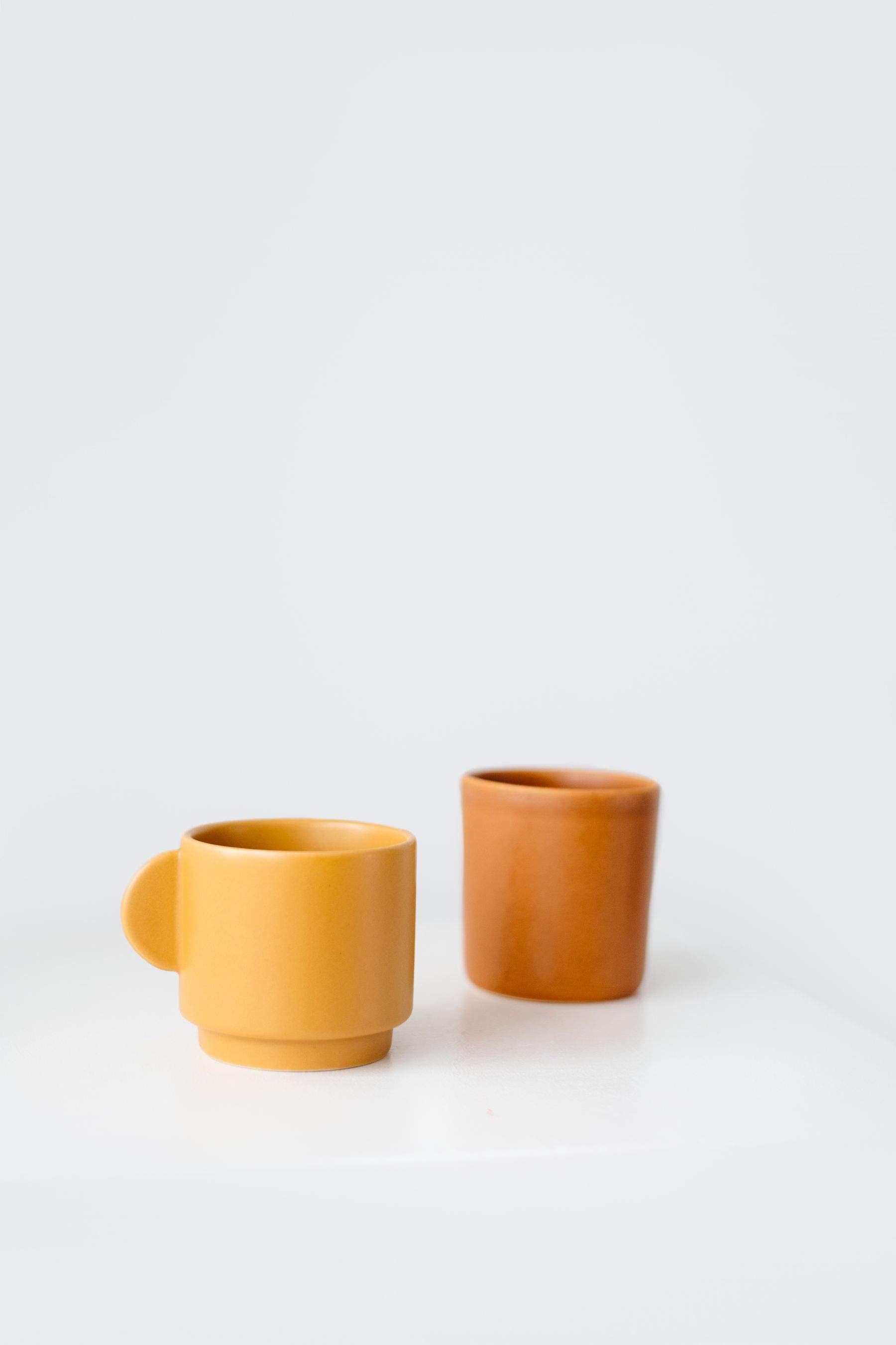 Two small ceramic cups in marigold and burnt orange glaze on a white table